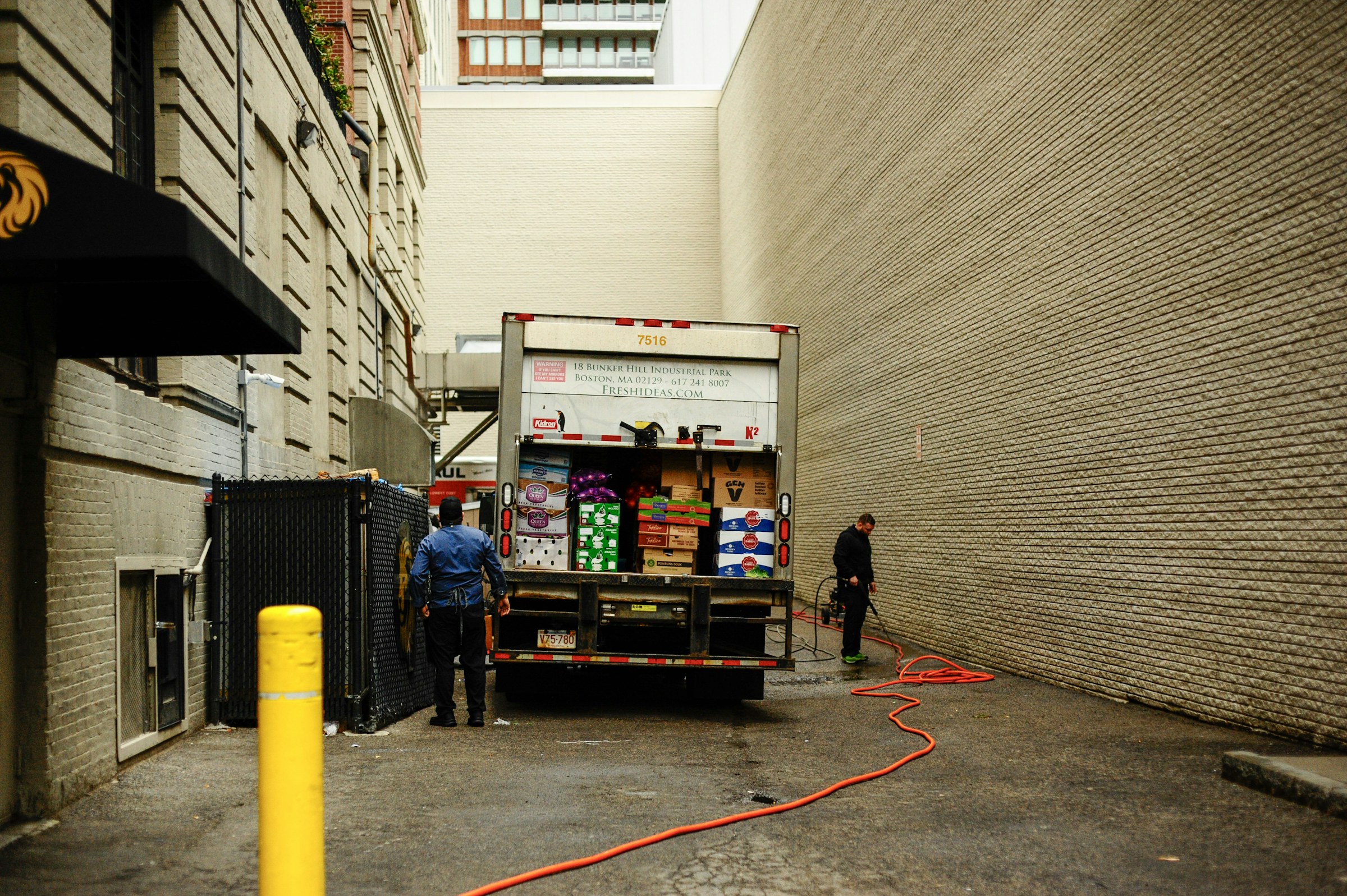 Workers unloading boxed produce from a truck in an urban service lane